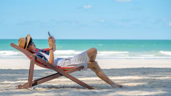 Eine Person hält ein Smartphone in der Hand und liegt am Strand in einer Liege.