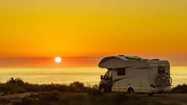 Wohnmobil steht beim Sonnenuntergang vor dem Meer