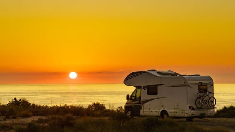 Wohnmobil steht beim Sonnenuntergang vor dem Meer