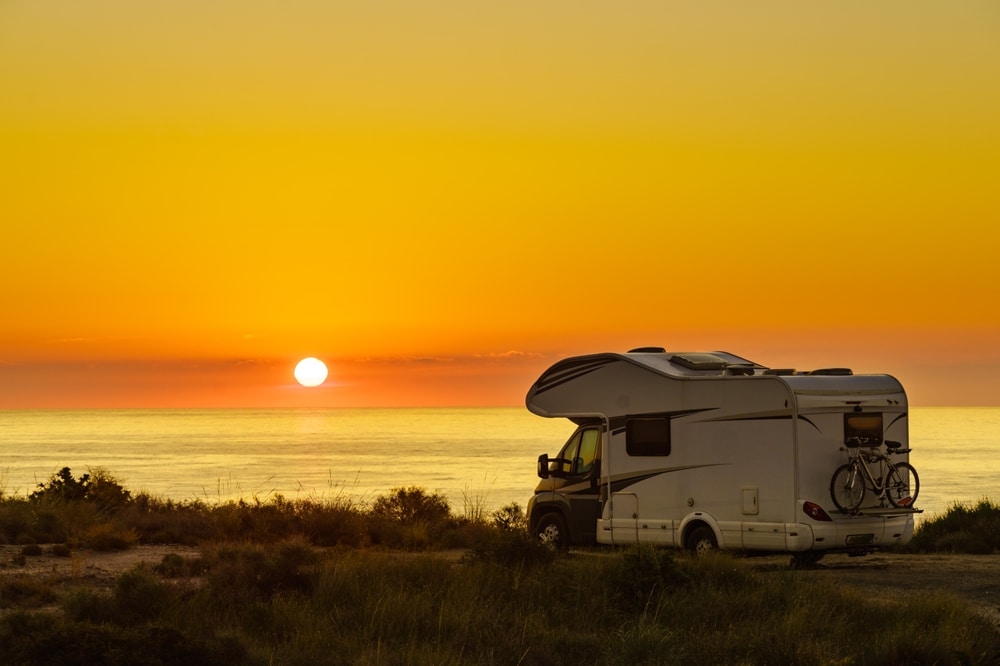 Wohnmobil steht beim Sonnenuntergang vor dem Meer