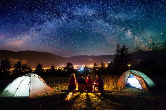 Zwei Paare sitzen in der Nacht vor ihren Zelten und beobachten den Nachthimmel