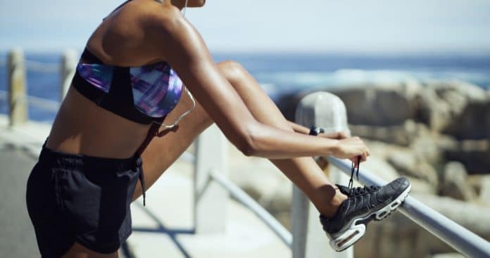 Hands,,Exercise,And,Tie,Shoelaces,At,Beach,,Promenade,Or,Prepare Frau schnürt Ihre Joggingschuhe, im Hintergrund ist das Meer zu sehen