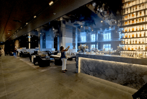 Eine Frau macht ein Foto in der Nähe einer modernen Bar mit einem hohen, hinterleuchteten Flaschenregal in einer eleganten Lounge mit Marmor und dunklen Möbeln.