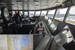 Moderne Schiffsbrücke mit mehreren Kontrollbildschirmen, Navigationsgeräten und großen Fenstern mit Blick auf einen Hafen. Zwei Personen sitzen dort. Eine Einblendung zeigt eine Nahaufnahme einer digitalen Seekarte mit detaillierten Hafeninformationen.