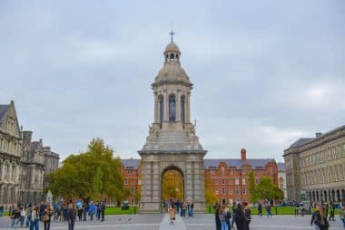 Der Glockenturm Campanile steht inmitten des mit Kopfsteinpflaster gepflasterten Innenhofs des Trinity College Dublin, umgeben von Studenten und historischen Gebäuden aus rotem Backstein.
