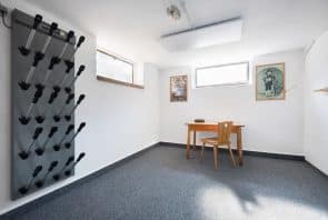 Ein graues Geräteregal, das an einer Wand in einem Raum befestigt ist, in dem sich ein Schreibtisch aus Holz, ein einzelner Stuhl und zwei gerahmte Drucke befinden.