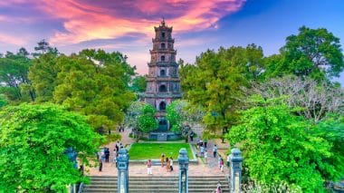 Die siebenstöckige Thien-Mu-Pagode, umgeben von Bäumen und Besuchern, vor dem Hintergrund eines leuchtenden Sonnenuntergangs.