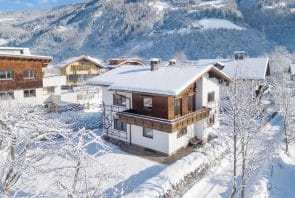 Ein schneebedecktes Berghaus mit Holzelementen, umgeben von schneebedeckten Bäumen und einer Berglandschaft.